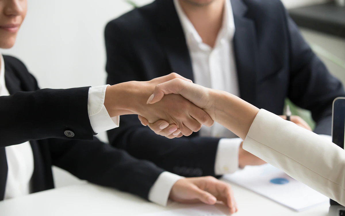 Two executives shaking hands across a conference table.